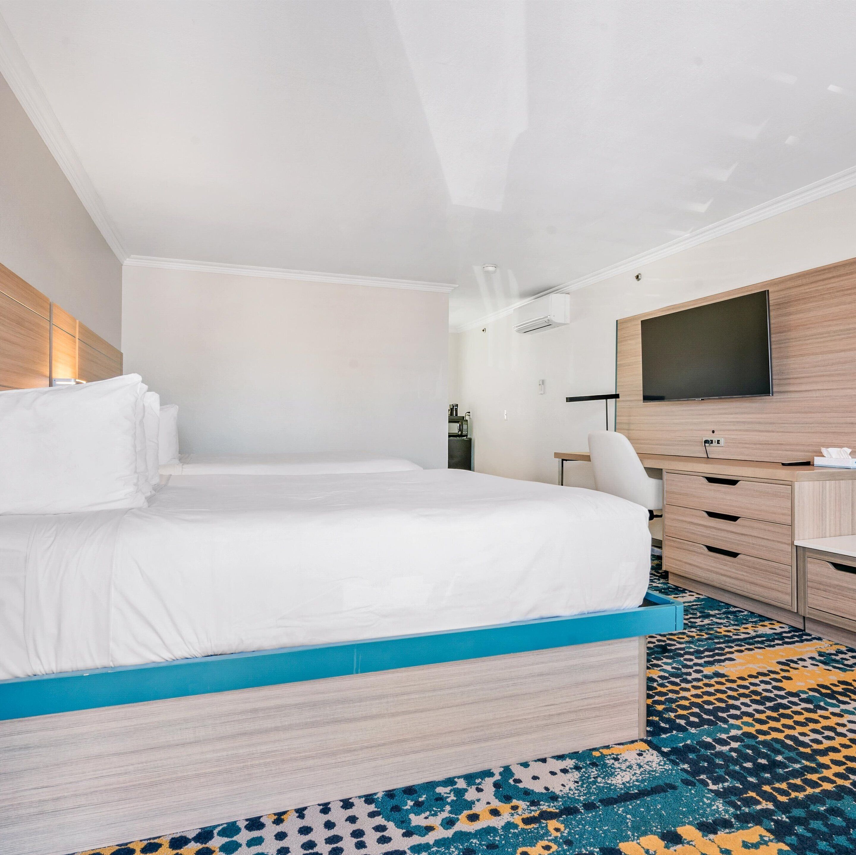Habitación de hotel con una cama grande, un escritorio, una silla, un televisor de pantalla plana y una alfombra estampada.