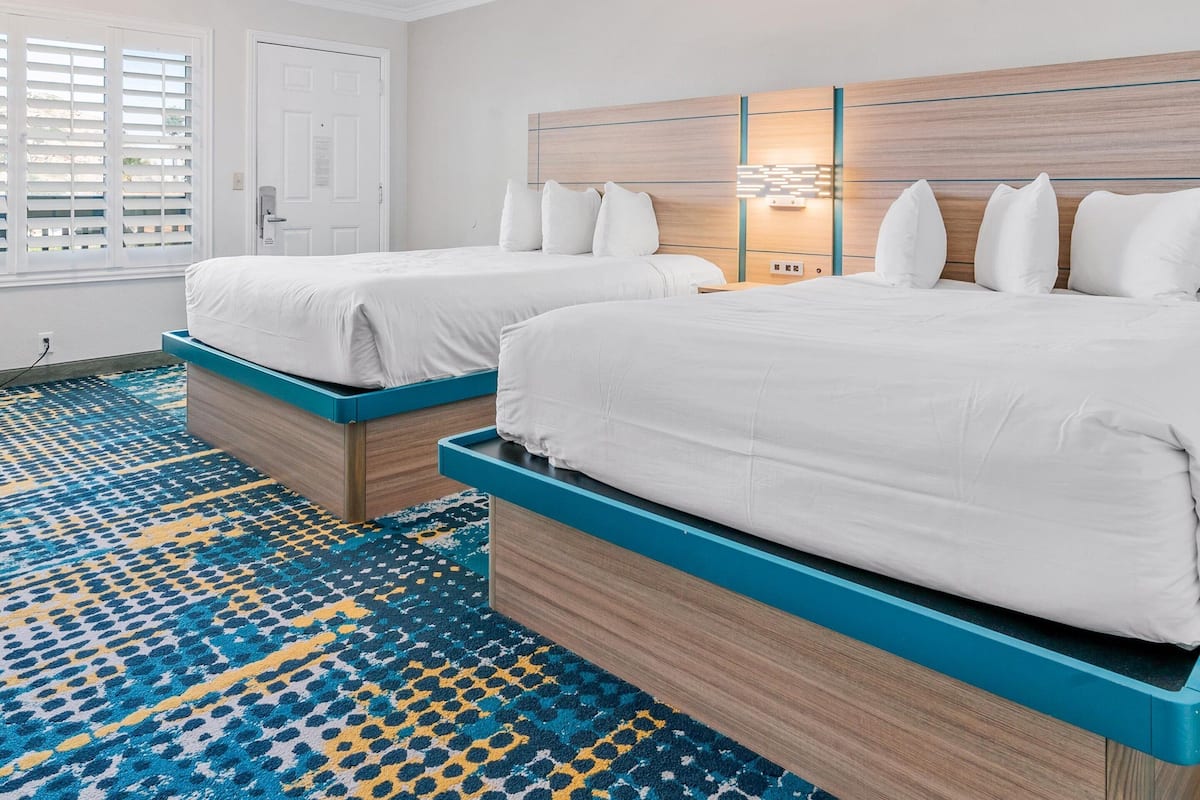 A hotel room with two beds, a patterned carpet, and a wooden headboard with built-in lighting.