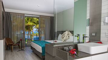 A hotel room with a bed, a bathroom with a large mirror, and a view of palm trees through the window.