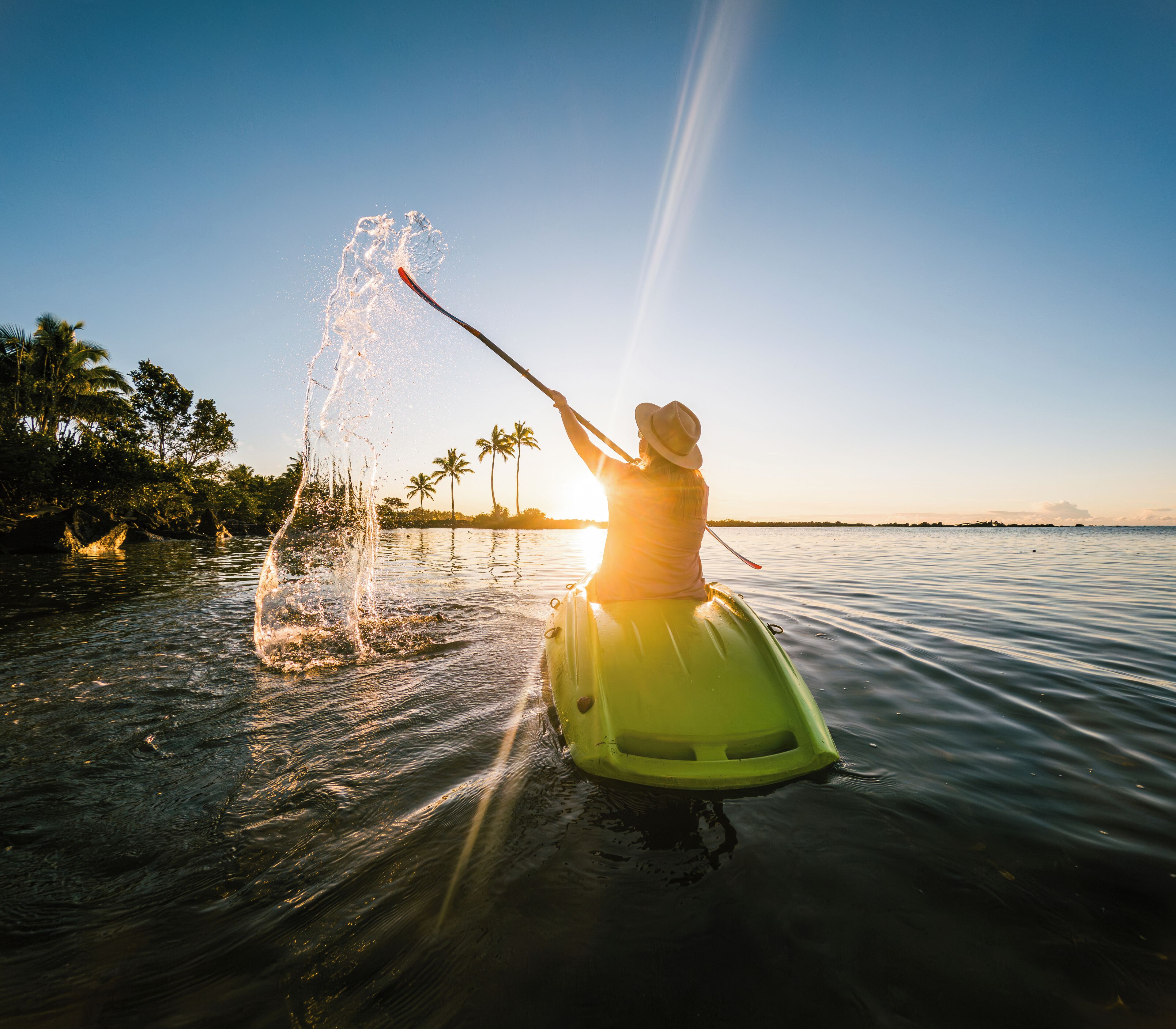 A person kayaking on calm water with a sunset in the background.