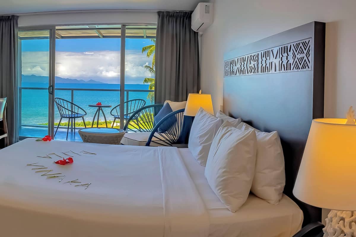 Een hotelkamer met een groot bed, een bureau, een televisie en een balkon met uitzicht op zee.
