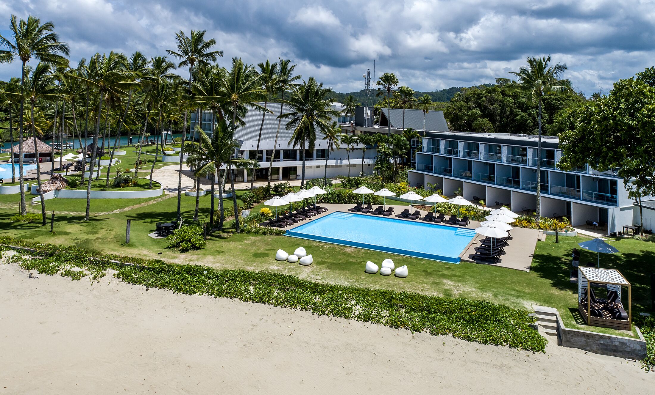 A resort with a swimming pool, lounge chairs, and palm trees.