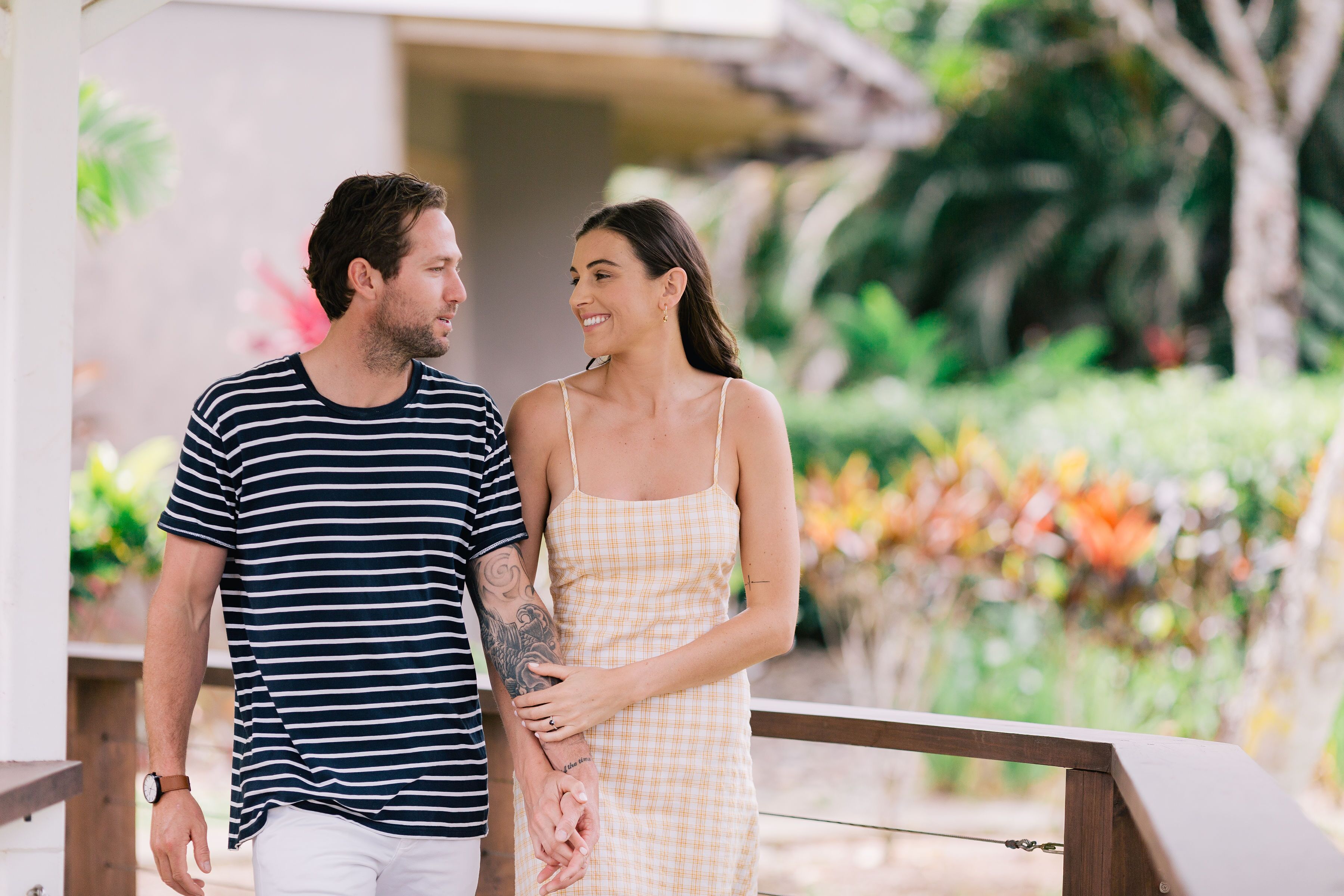 A couple holding hands on a wooden deck with a garden in the background.