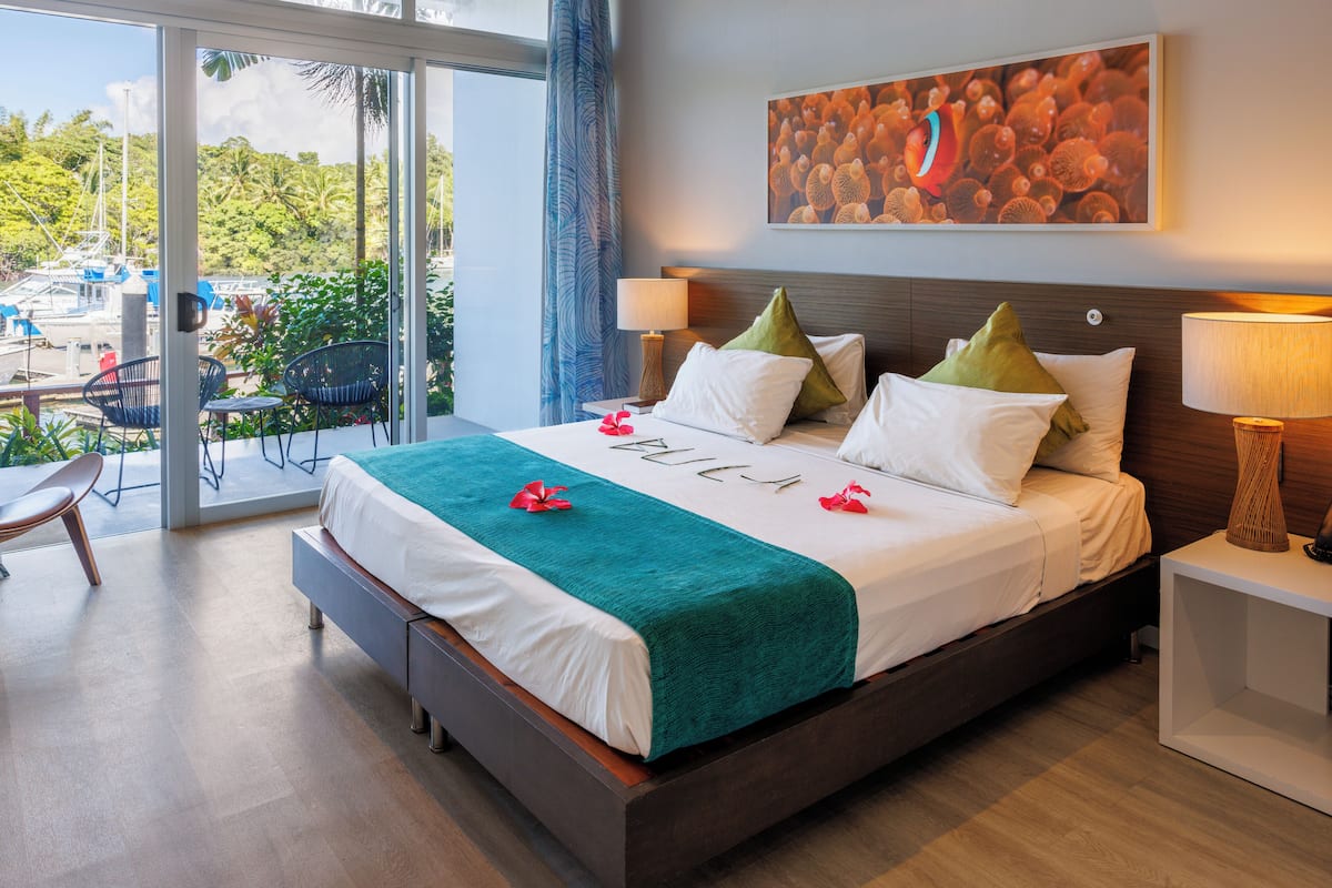 Een moderne hotelkamer met een groot bed, uitzicht op de omgeving en een tropisch schilderij aan de muur.
