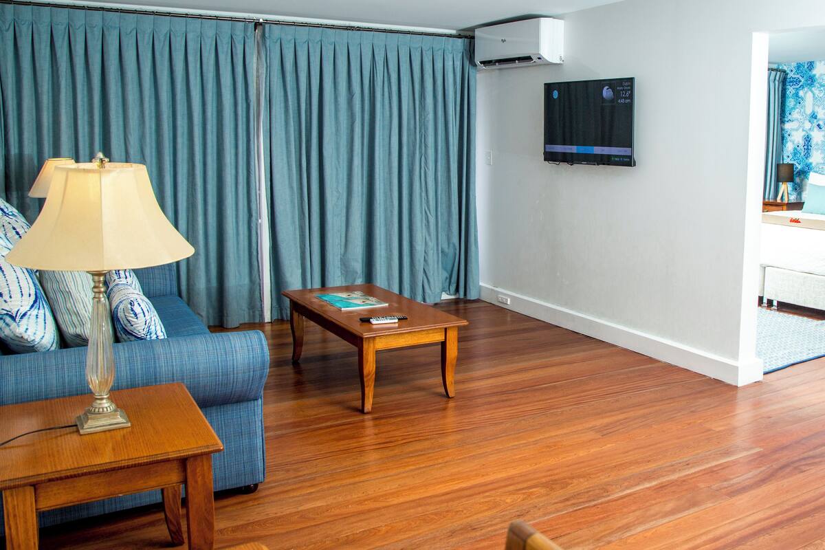 Een moderne woonkamer met een bank, salontafel en een aan de muur bevestigde televisie.