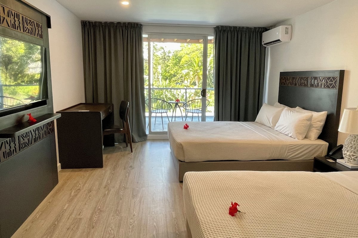 Een hotelkamer met twee bedden, een bureau en een balkon met uitzicht op groen.