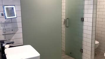 Et moderne badeværelse med et stort spejl, en hvid vask og et bruseområde med glasvægge.