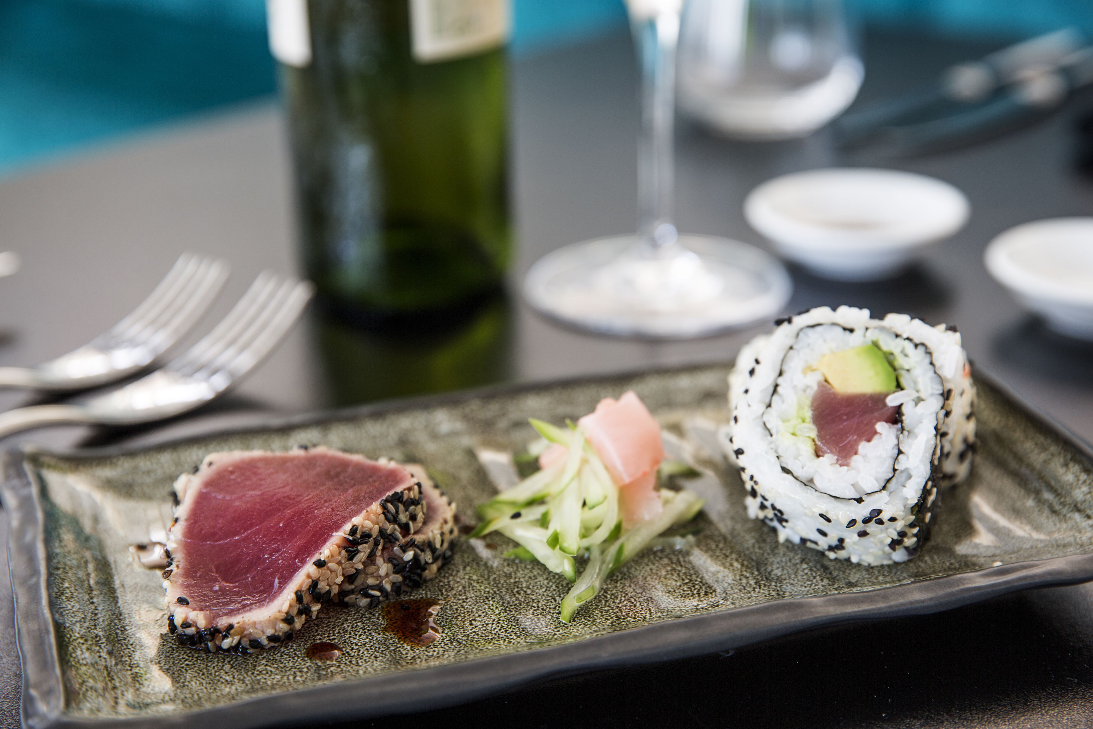 A plate of sushi and a bottle of wine on a table.
