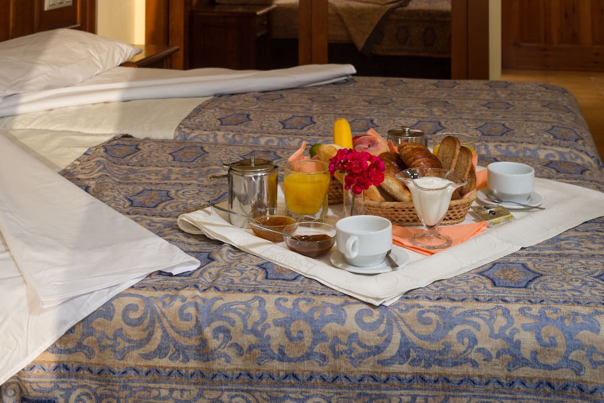 Ein Hotelzimmer mit einem aufgeräumten Bett, einem Frühstücksbrett auf dem Bett und einem Spiegel, der den Raum reflektiert.
