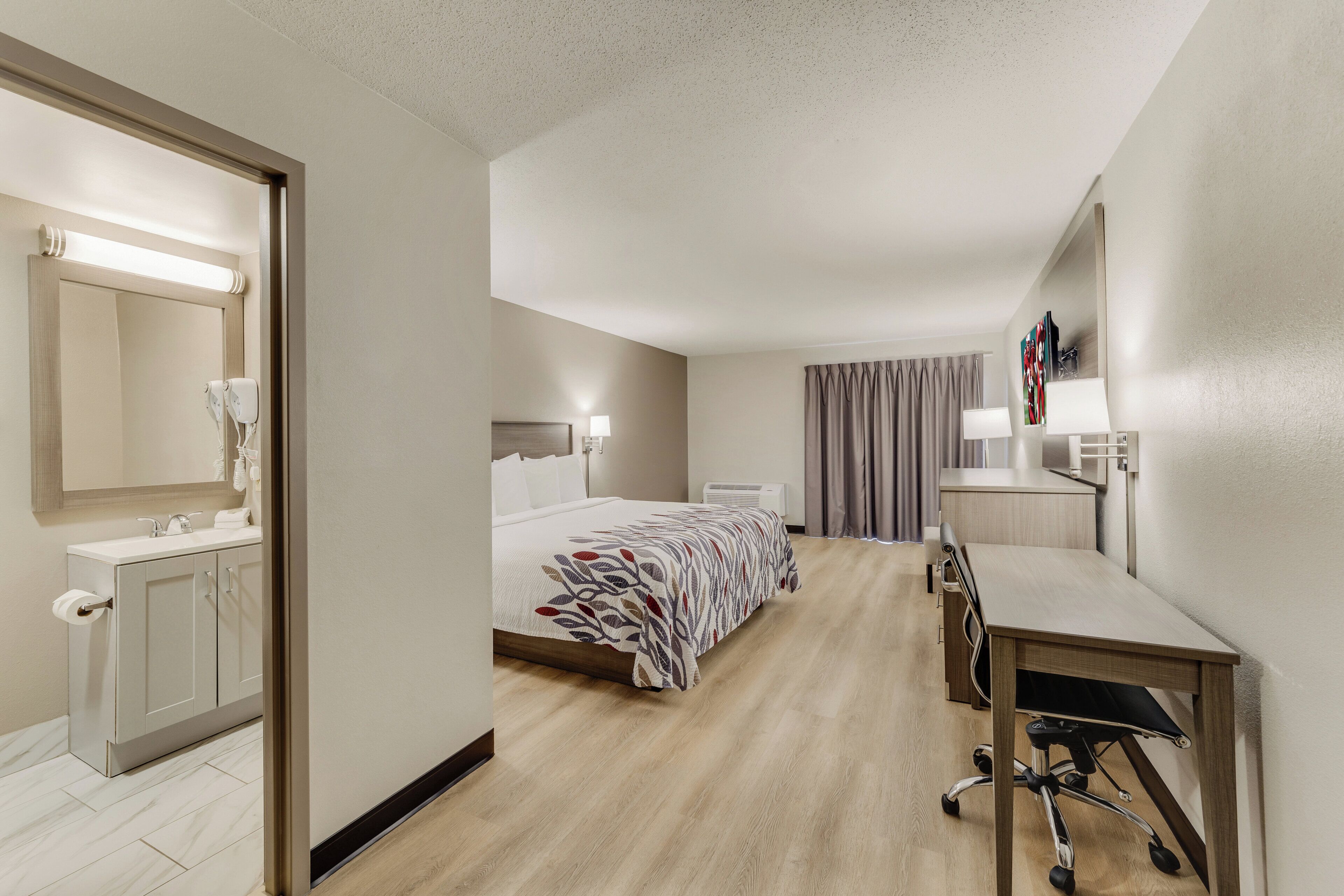 Ein Hotelzimmer mit Bett, Schreibtisch, Spiegel, Badezimmer mit Waschbecken und Dusche.