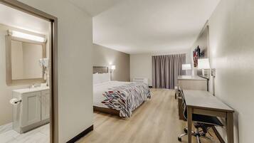 Ein Hotelzimmer mit Bett, Schreibtisch, Spiegel, Badezimmer mit Waschbecken und Dusche.