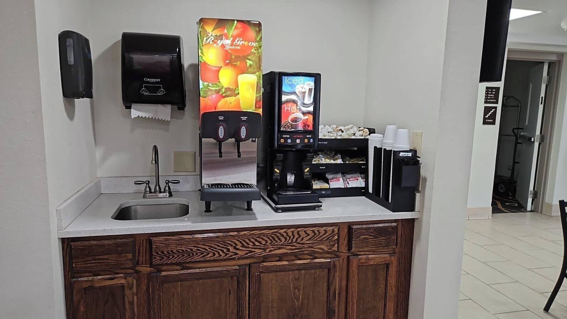 Un espace de libre-service proposant des boissons, avec une machine à café, un distributeur de jus et un présentoir réfrigéré.
