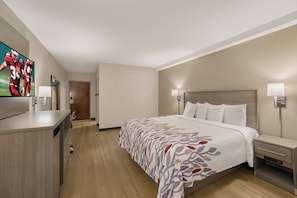 Habitación de hotel con cama, lámparas de noche, televisión, escritorio y una puerta que da a otra habitación.