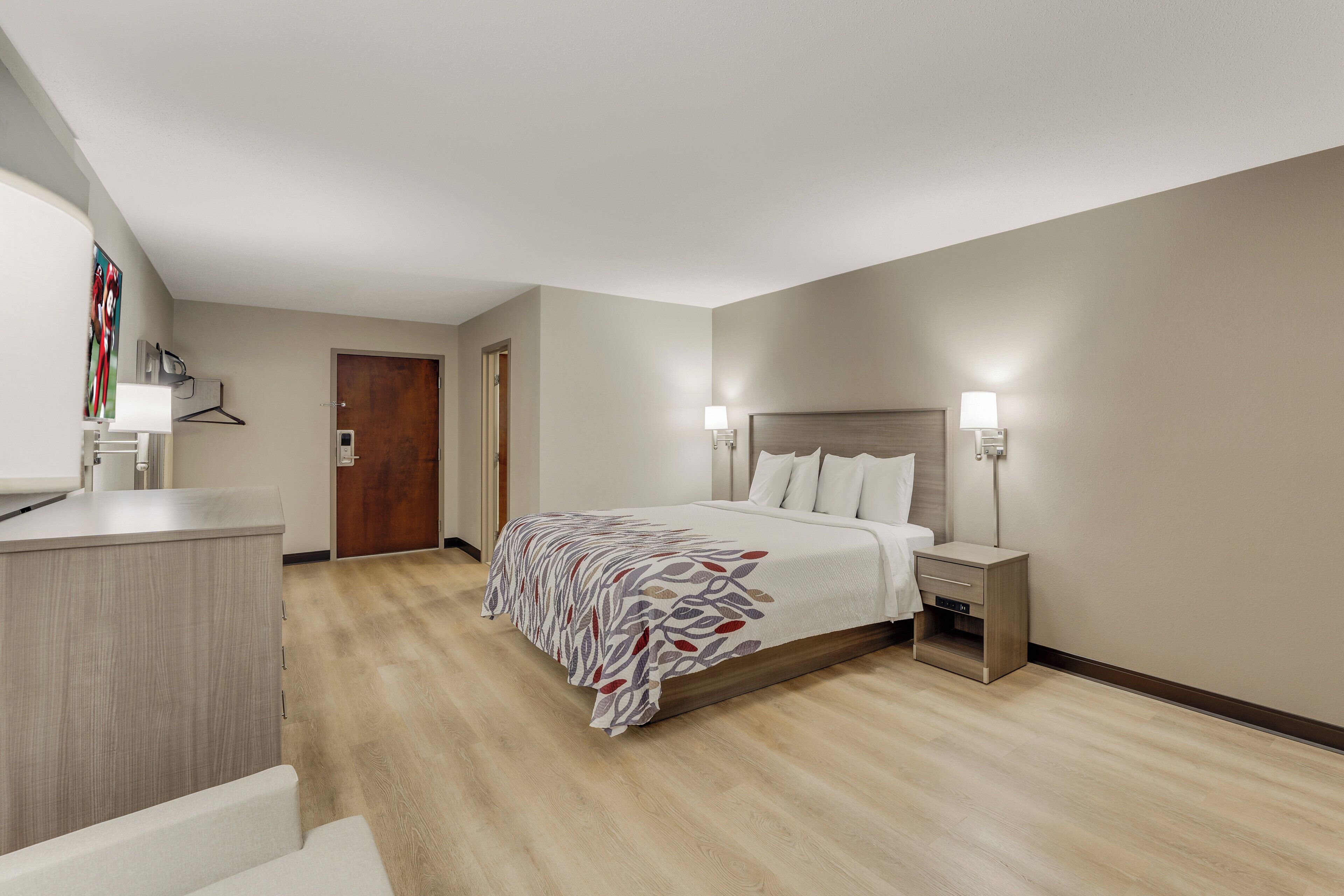 A hotel room with a bed, bedside lamps, a desk, and a door.