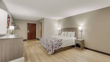 A hotel room with a bed, bedside lamps, a desk, and a door.