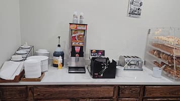 Una barra de desayuno con cafetera, dispensador de sirope para gofres, tostadora y una variedad de pasteles.