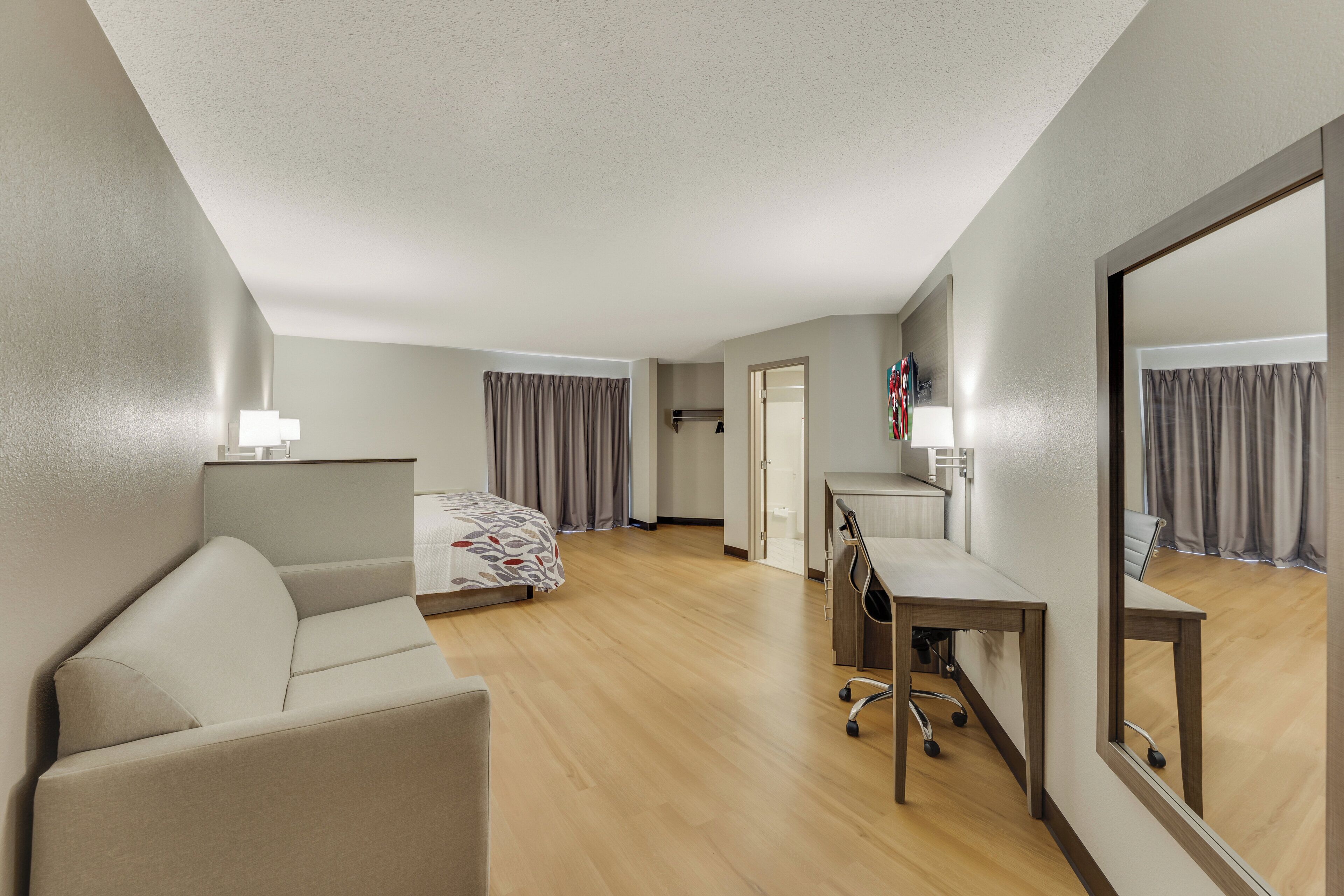Una camera d'albergo con un letto, una scrivania, una sedia, uno specchio e una lampada.