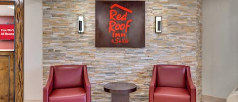 A lobby with a stone wall, two red leather chairs, a small table, and a sign reading 'Red Roof Inn Suites'.