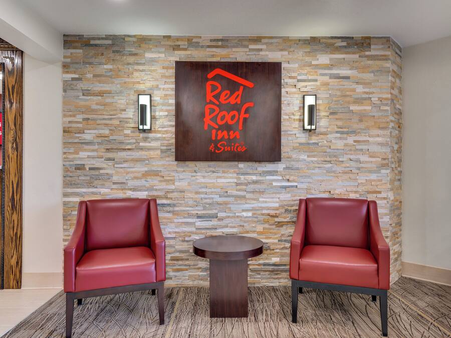 A lobby with a stone wall, two red leather chairs, a small table, and a sign reading 'Red Roof Inn Suites'.