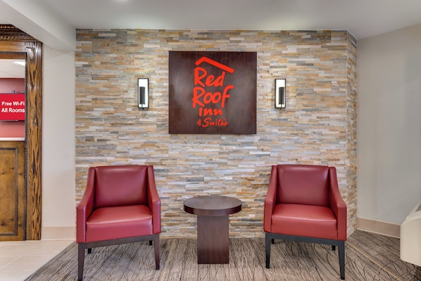 Un hall con pared de piedra, dos sillones de cuero rojo, una mesita y un letrero que dice 'Red Roof Inn Suites'.