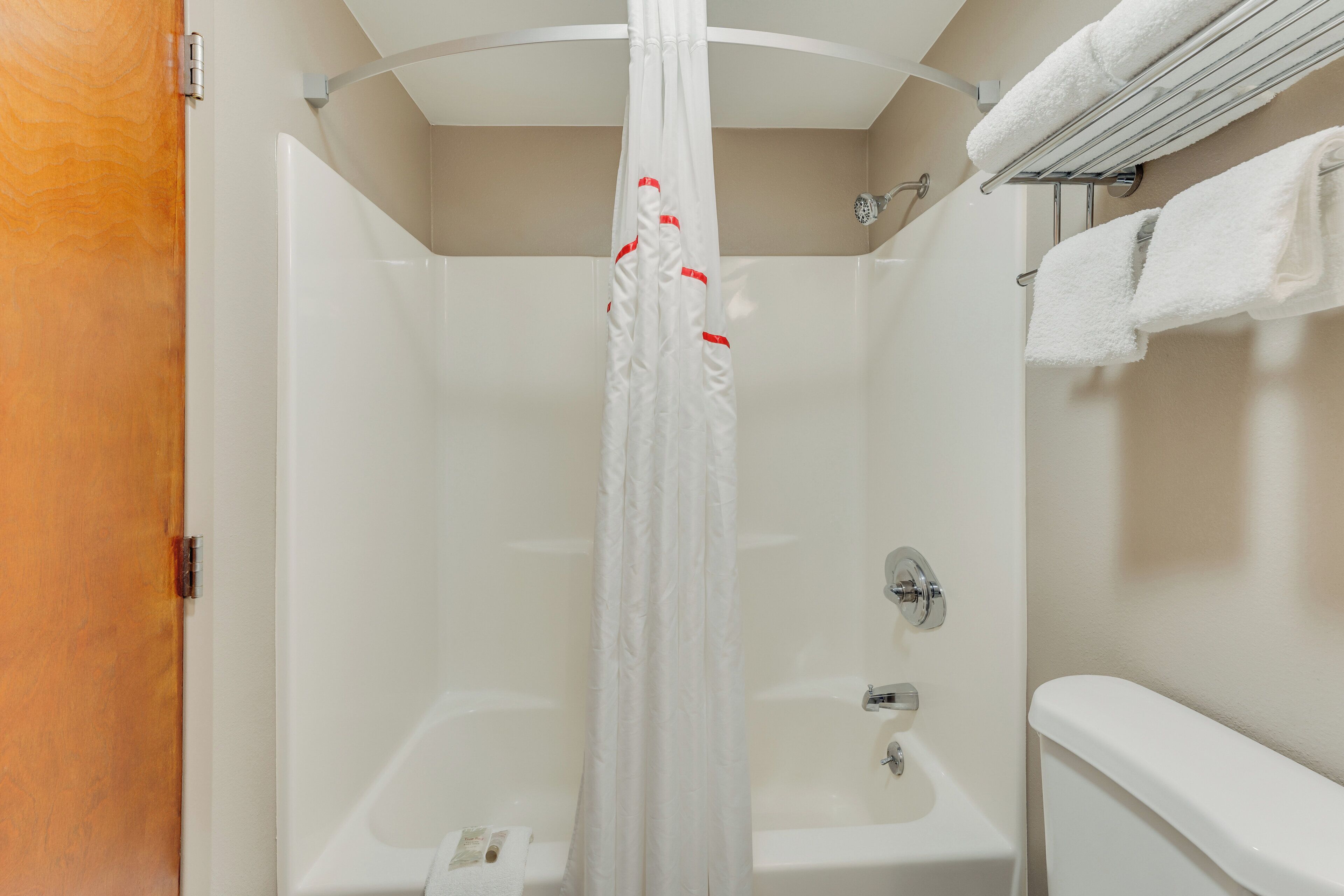 Een douche met gordijn, een bad en een handdoekrek met handdoeken.