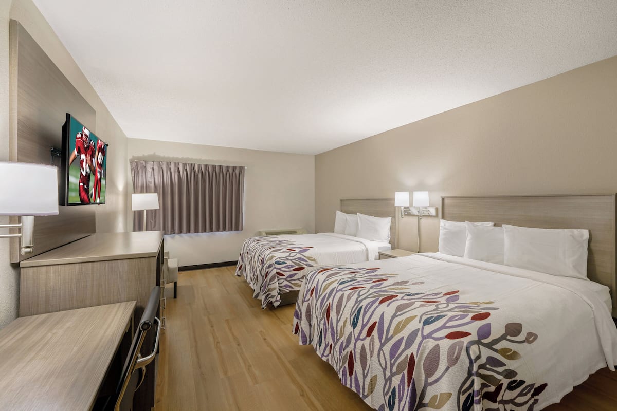A hotel room with two beds, a desk with a chair, a television, and a window with curtains.