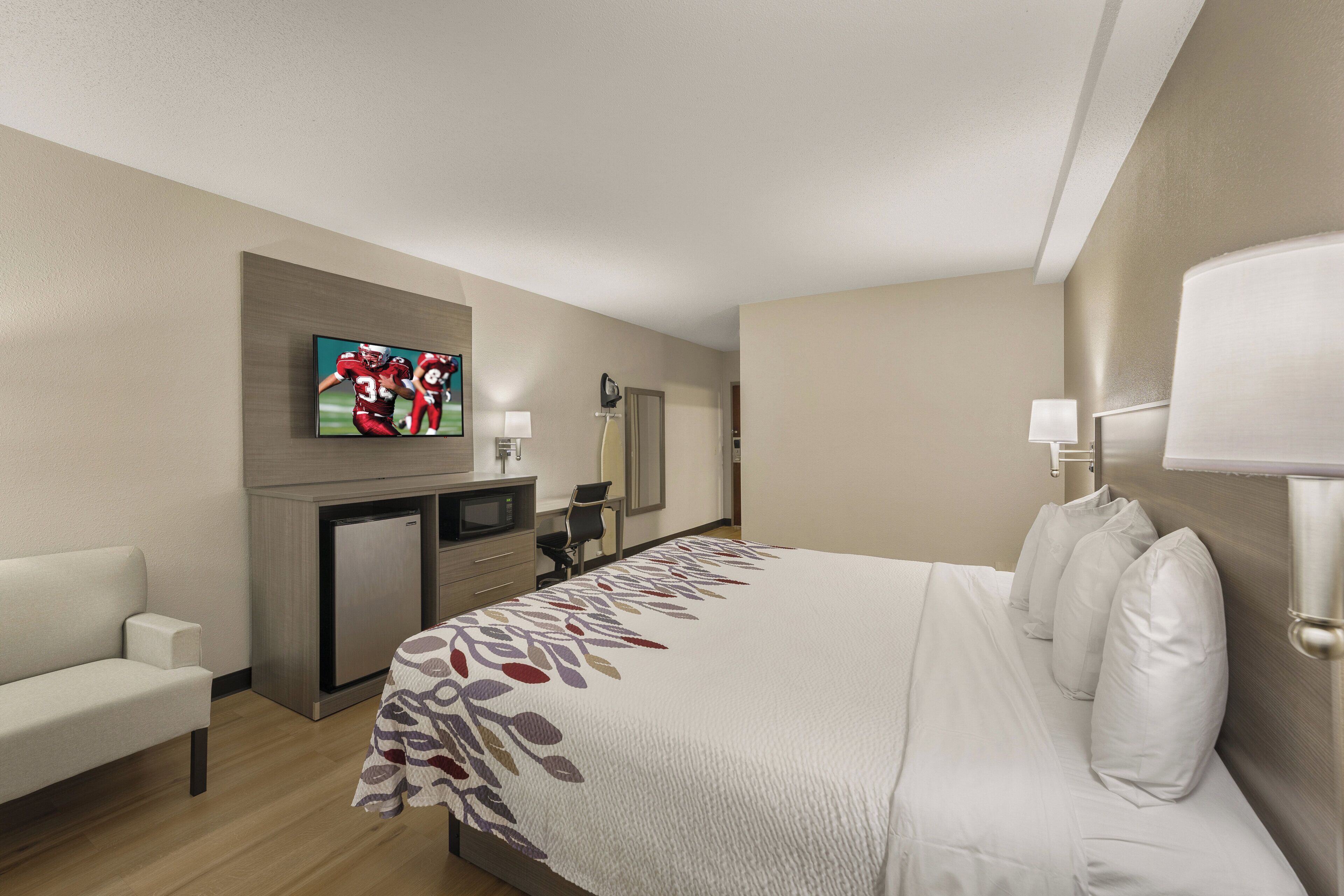 A hotel room with a bed, a desk with a computer, a television, and a microwave.
