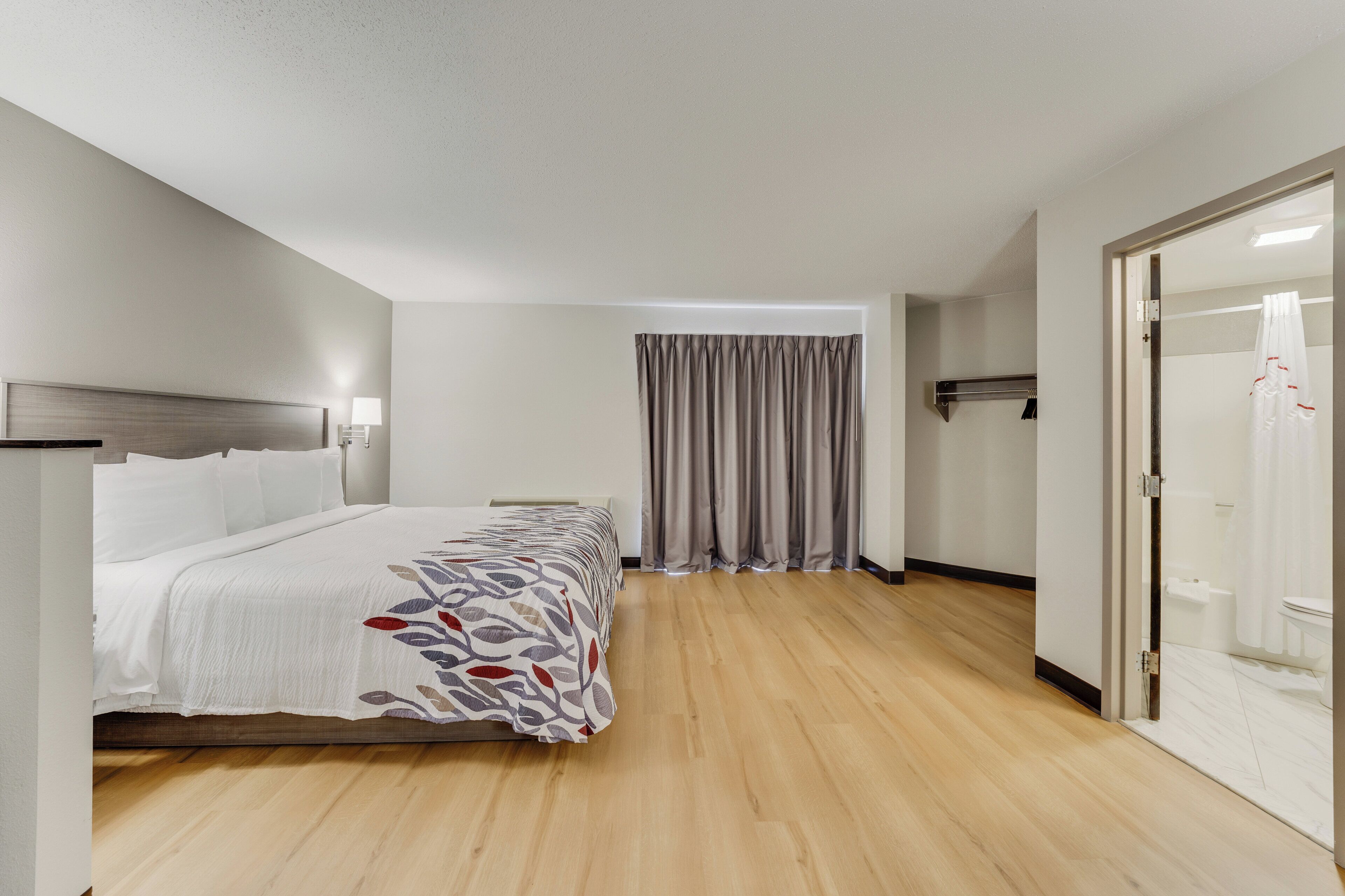 A hotel room with a bed, a nightstand, a lamp, a shower area, and a door.