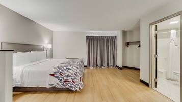 A hotel room with a bed, a nightstand, a lamp, a shower area, and a door.