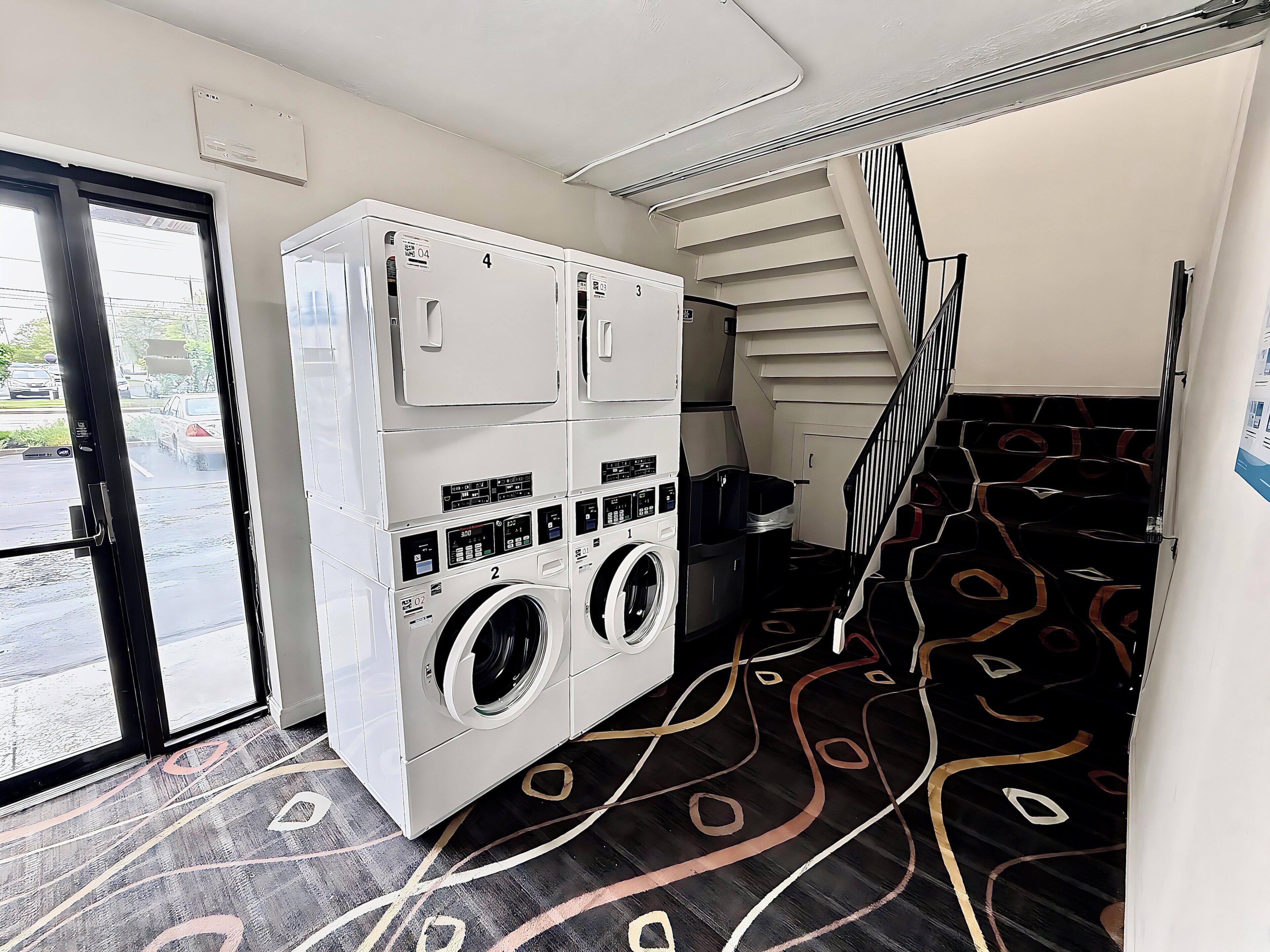 A laundry room with stacked washers and dryers, a staircase, and a patterned floor.