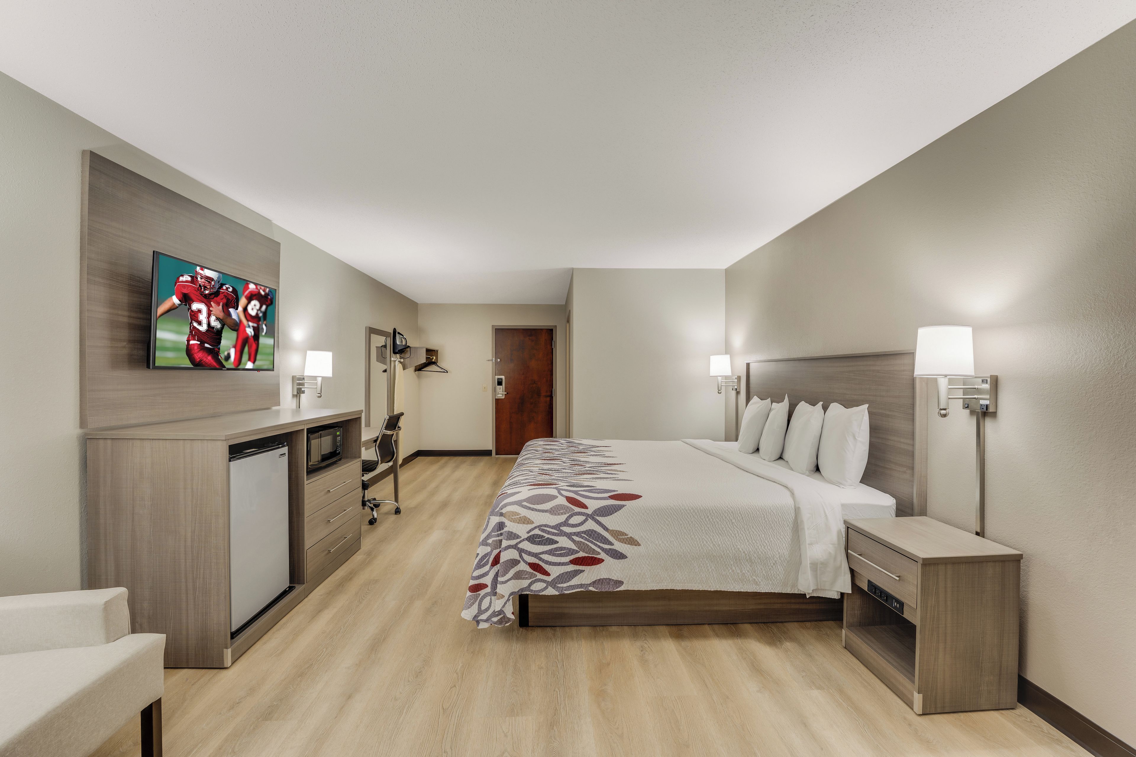 A hotel room with a bed, bedside tables, a TV, a desk with a microwave, and a wardrobe.