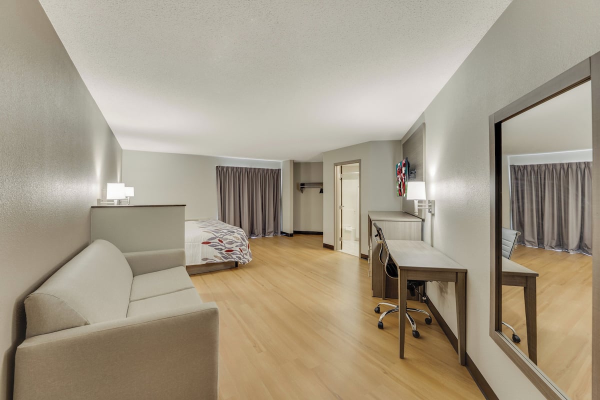 A hotel room with a bed, a desk, a chair, a lamp, and a large mirror.