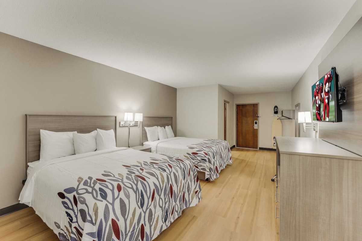 A hotel room with two beds, a desk, and a television.
