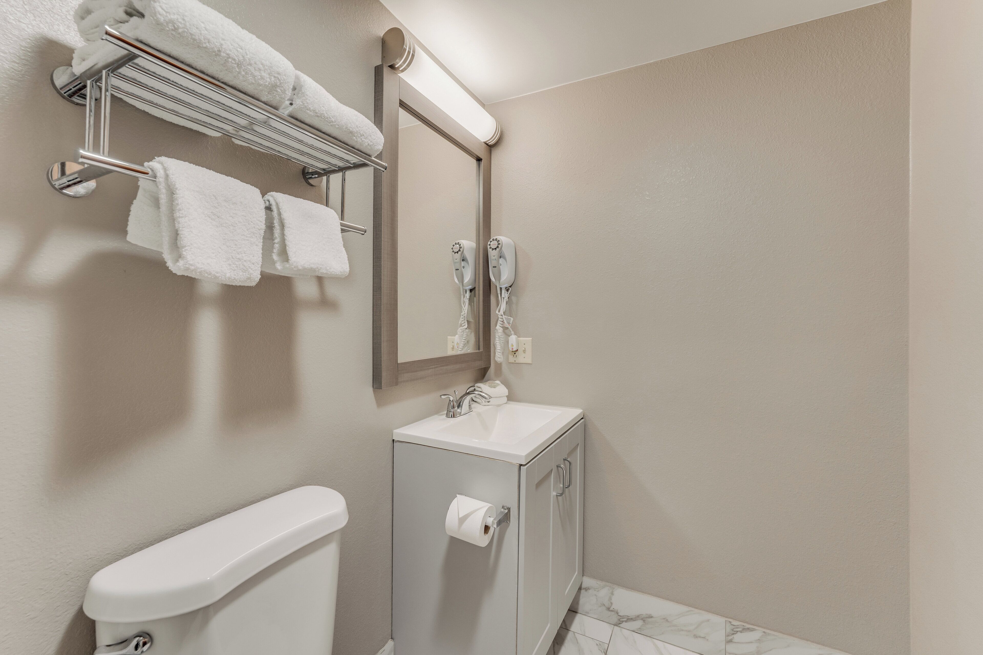 Un baño con inodoro, lavamanos, toallero y espejo.