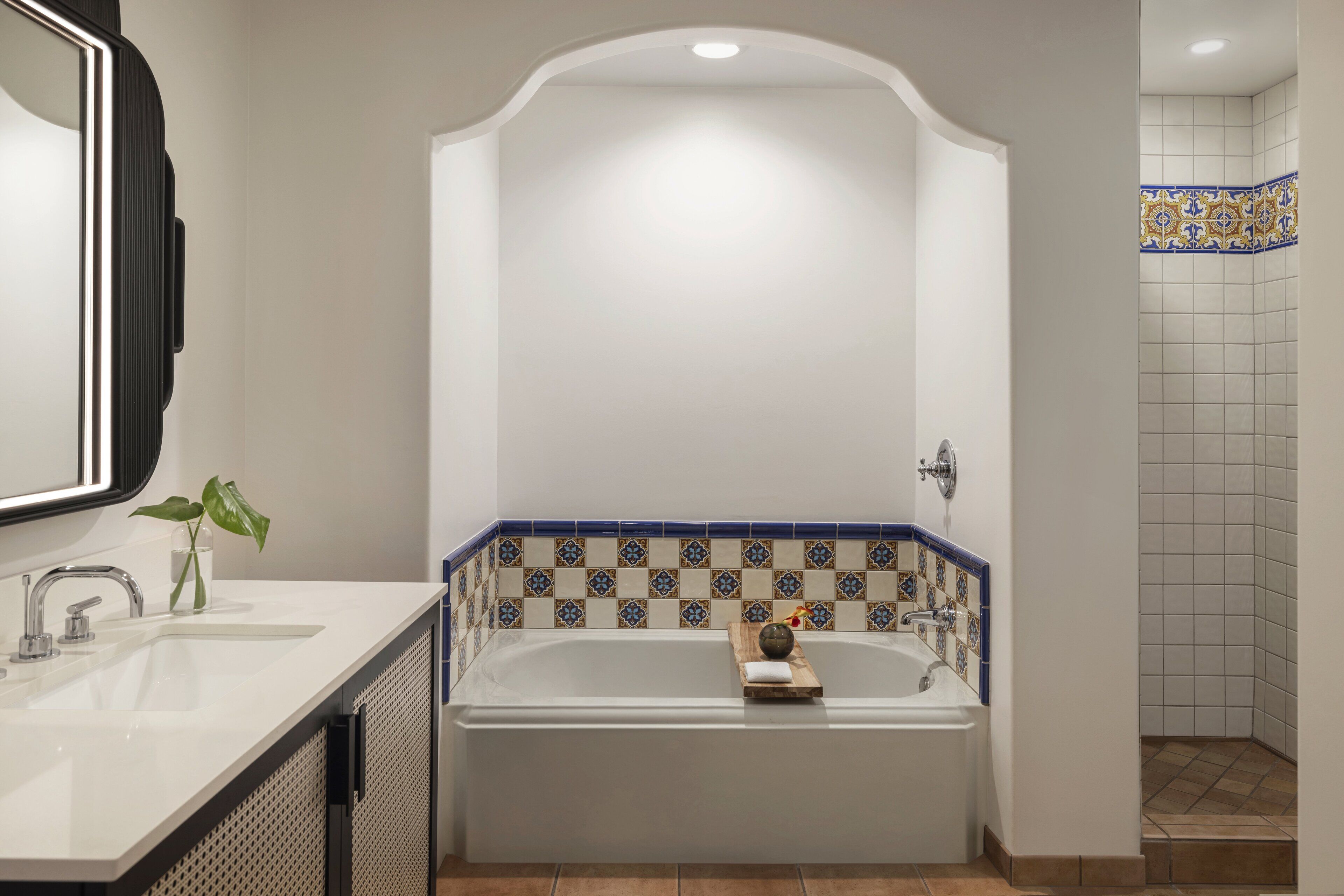 A bathroom with a white sink, a bathtub with a wooden tray, and a shower area with patterned tiles.