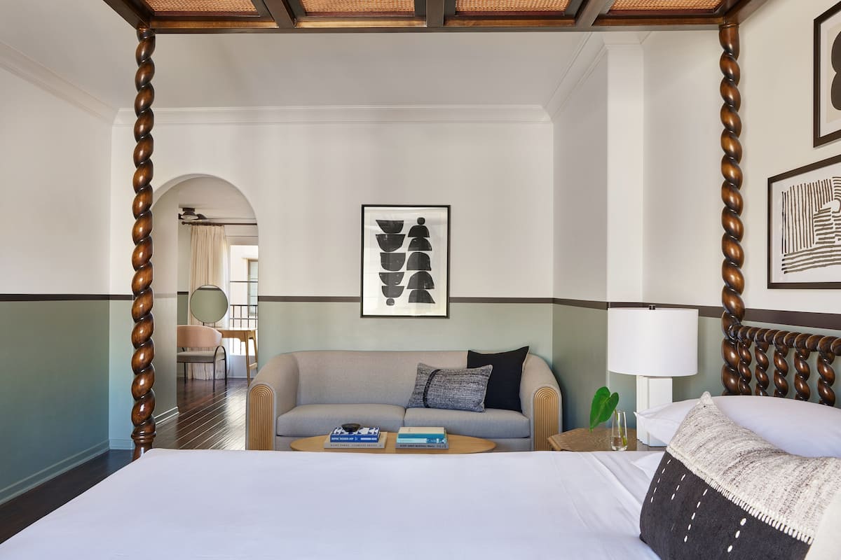 Una habitació d'hotel amb un llit gran, un sofà, una taula de cafè amb llibres, una làmpada i obra pictòrica emmarcada a les parets.