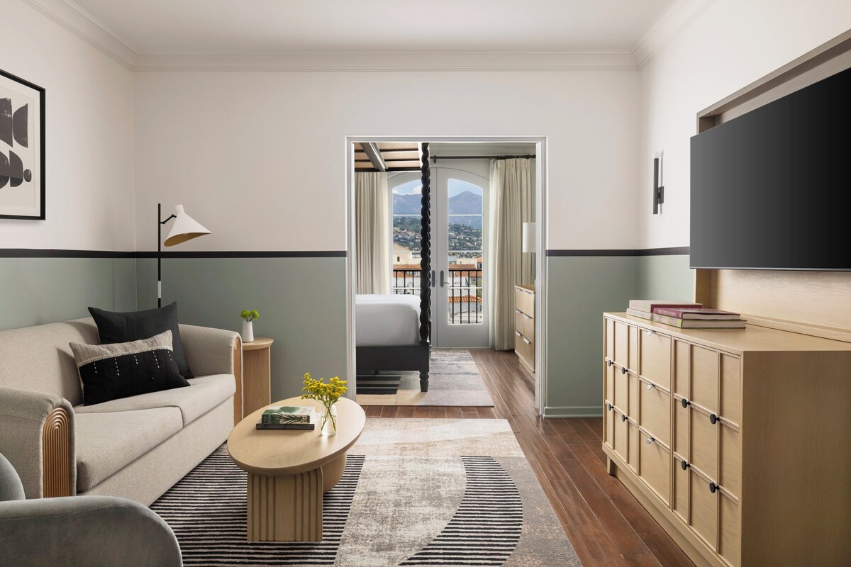 A modern living room with a sofa, coffee table, and a view through a doorway to a balcony.