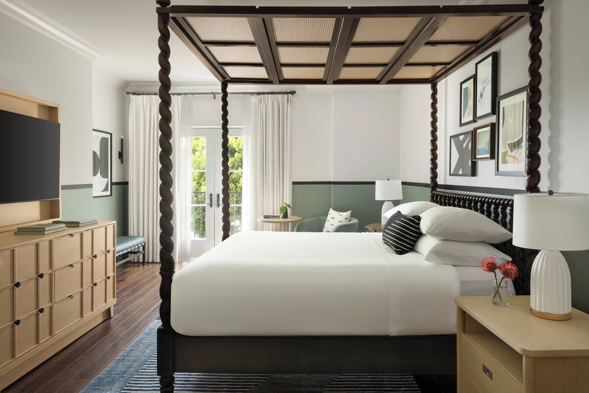 A four-poster bed with a canopy, a bedside table with a lamp, and a television on a stand.