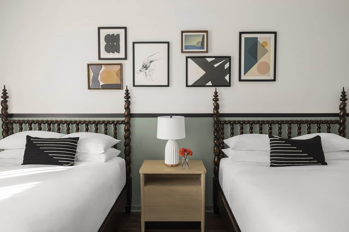Una habitació d'hotel amb dos llits, una nit de nit amb una làmpada i quatre quadres amb marc a la paret.