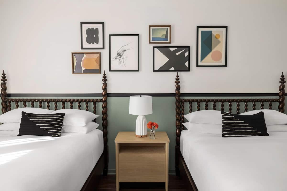 Habitació d'hotel amb dos llits, una tauleta de nit amb làmpada i una obra d'art a la paret.