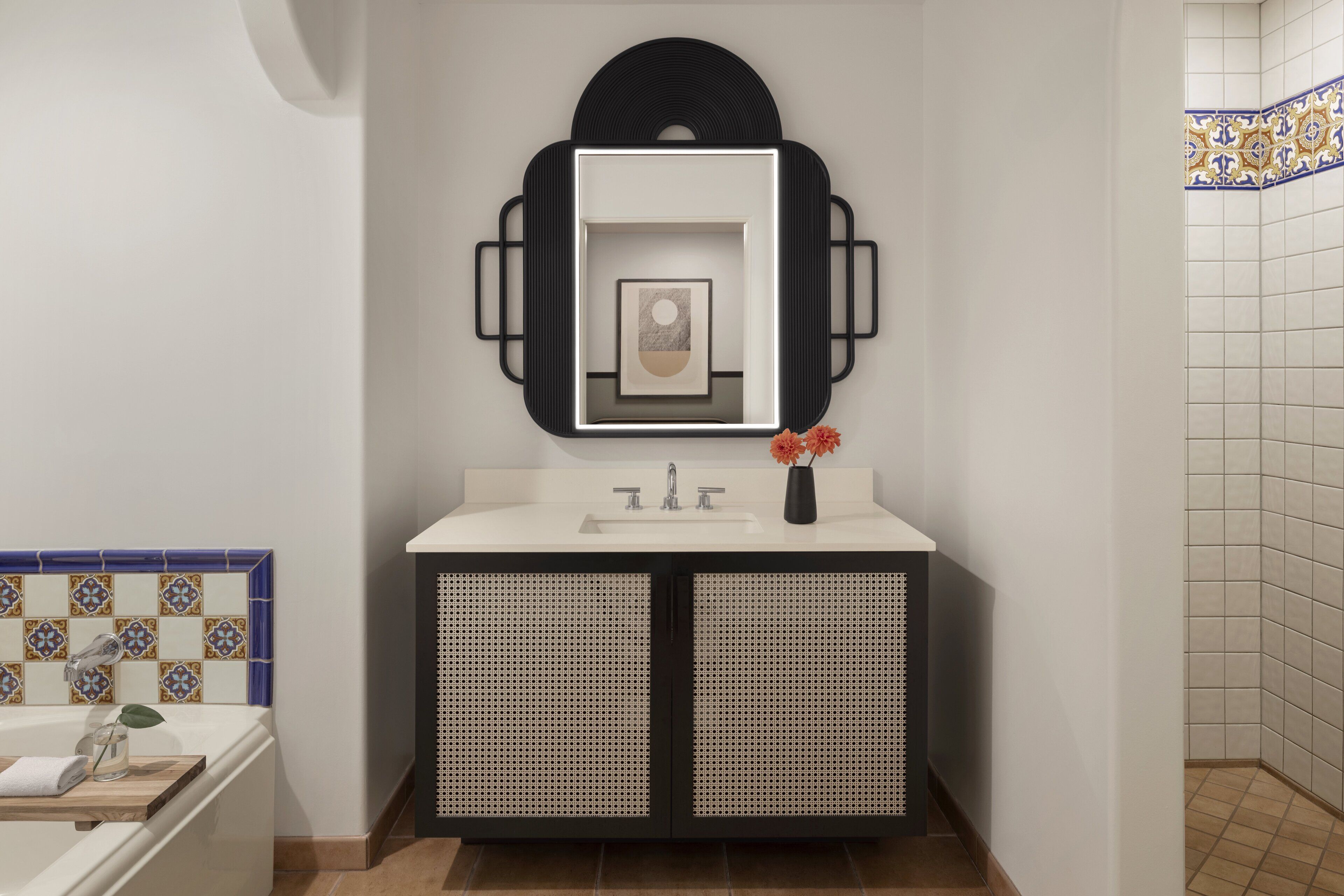 A modern bathroom with a white sink, black cabinet, and a decorative mirror.