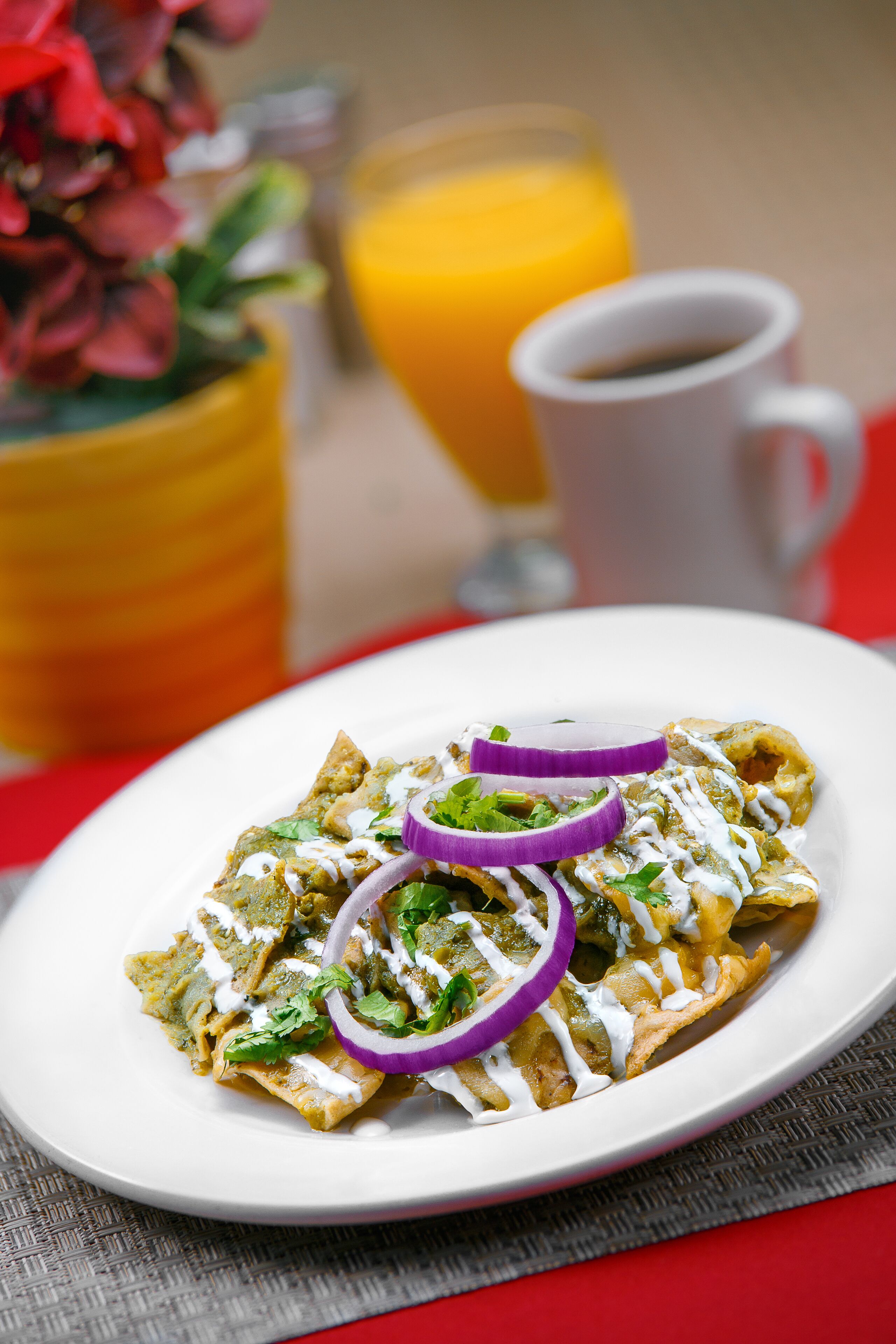 Un plato de comida con una taza blanca y un vaso de jugo de naranja al fondo.
