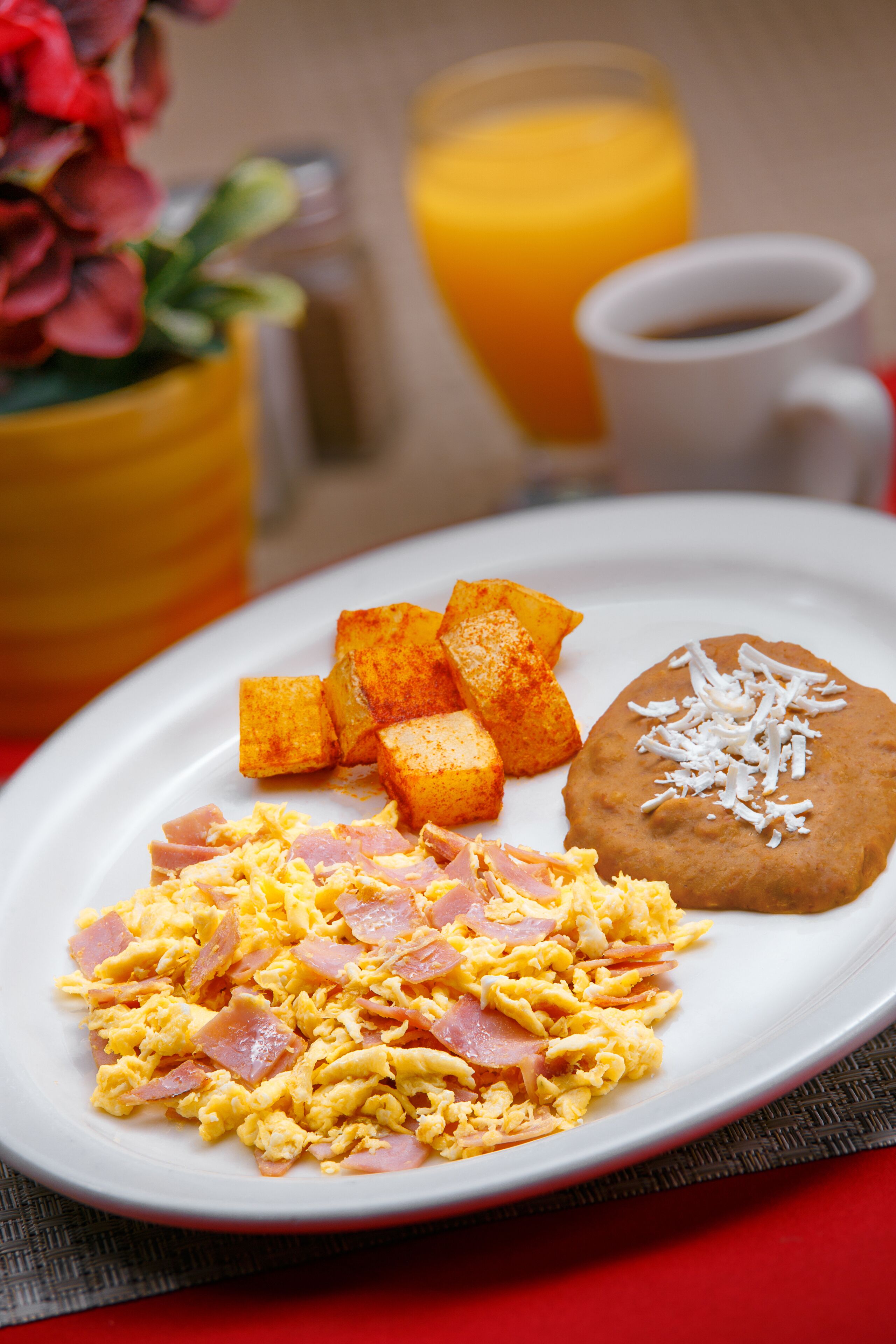 Un piatto con uova strapazzate, prosciutto e fagioli fritti, accompagnato da succo d'arancia e caffè.