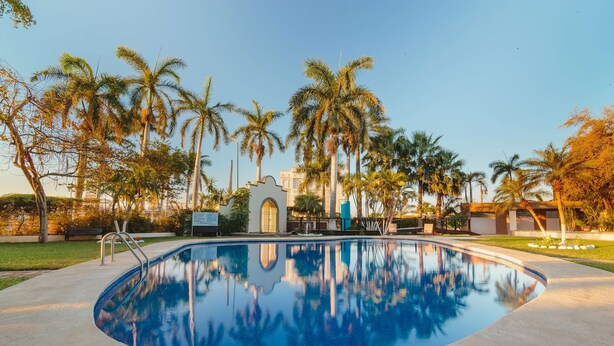 A swimming pool surrounded by palm trees and a building with a curved facade. - Best Western Plus San Jorge (Cajeme)