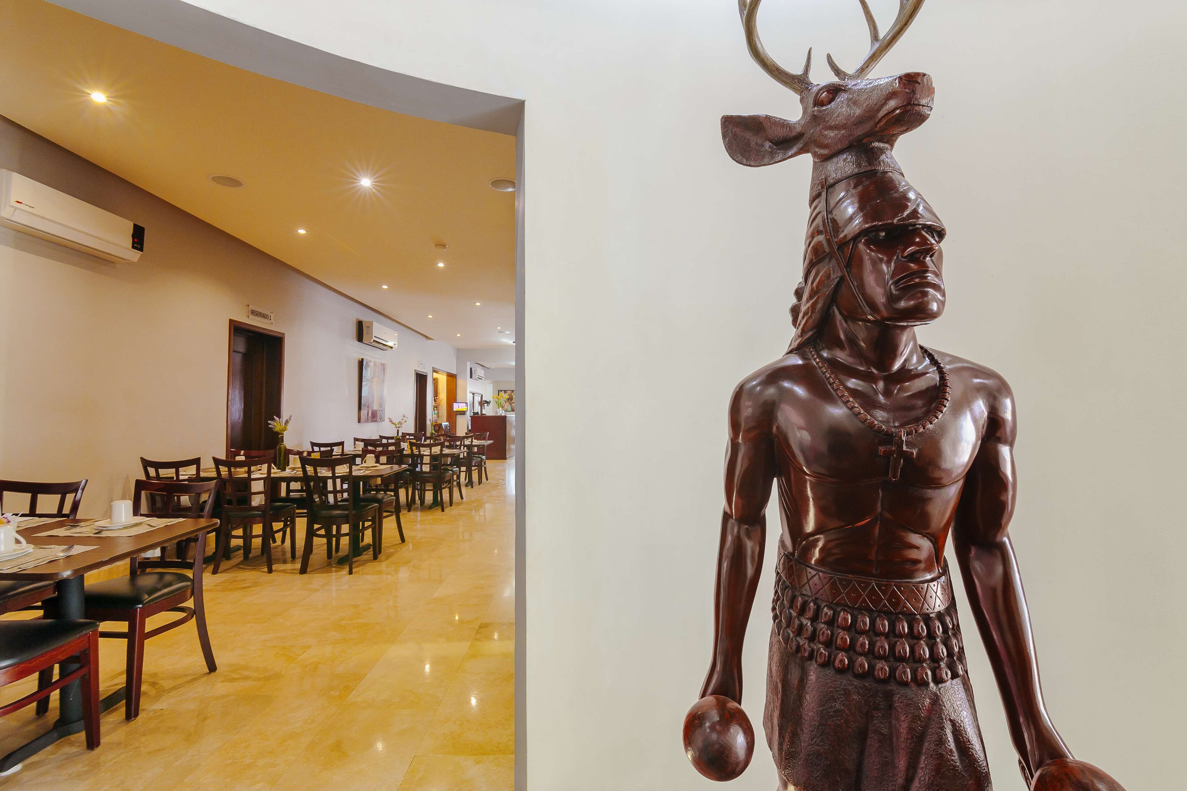 A statue of a muscular figure with antlers in a modern interior space with tables and chairs.