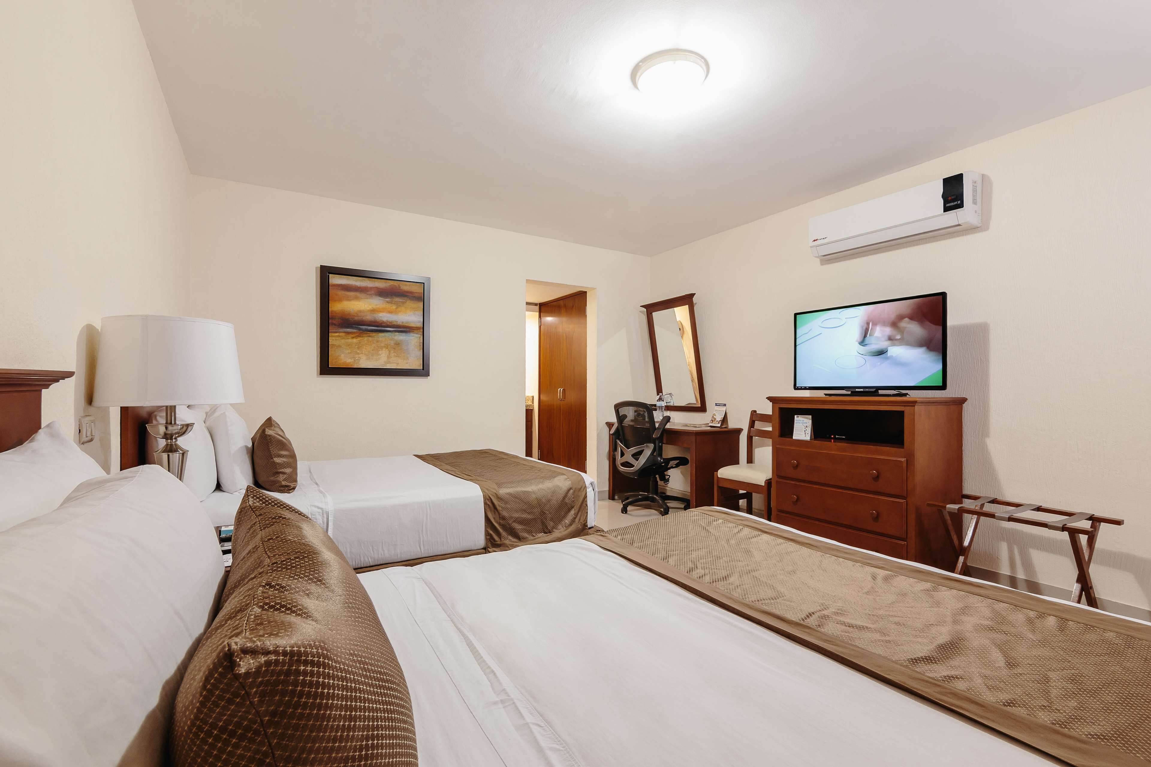 Ein Hotelzimmer mit zwei Betten, einem Schreibtisch, einem Stuhl, einem Fernseher und einer Klimaanlage.