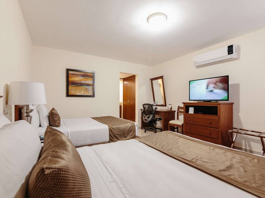 Ein Hotelzimmer mit zwei Betten, einem Schreibtisch, einem Stuhl, einem Fernseher und einer Klimaanlage.