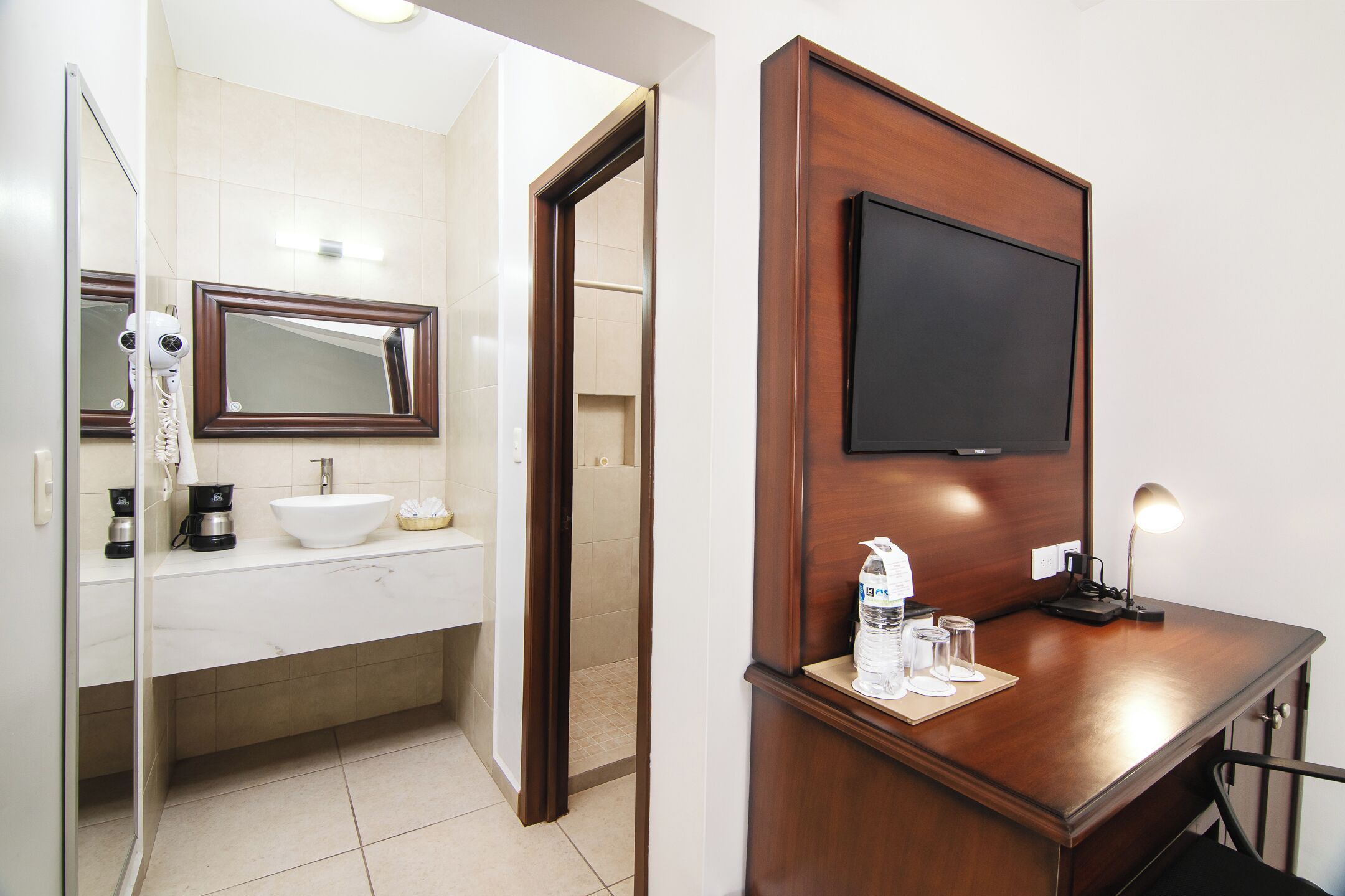 Un baño con lavamanos, espejo y televisor montado en la pared.