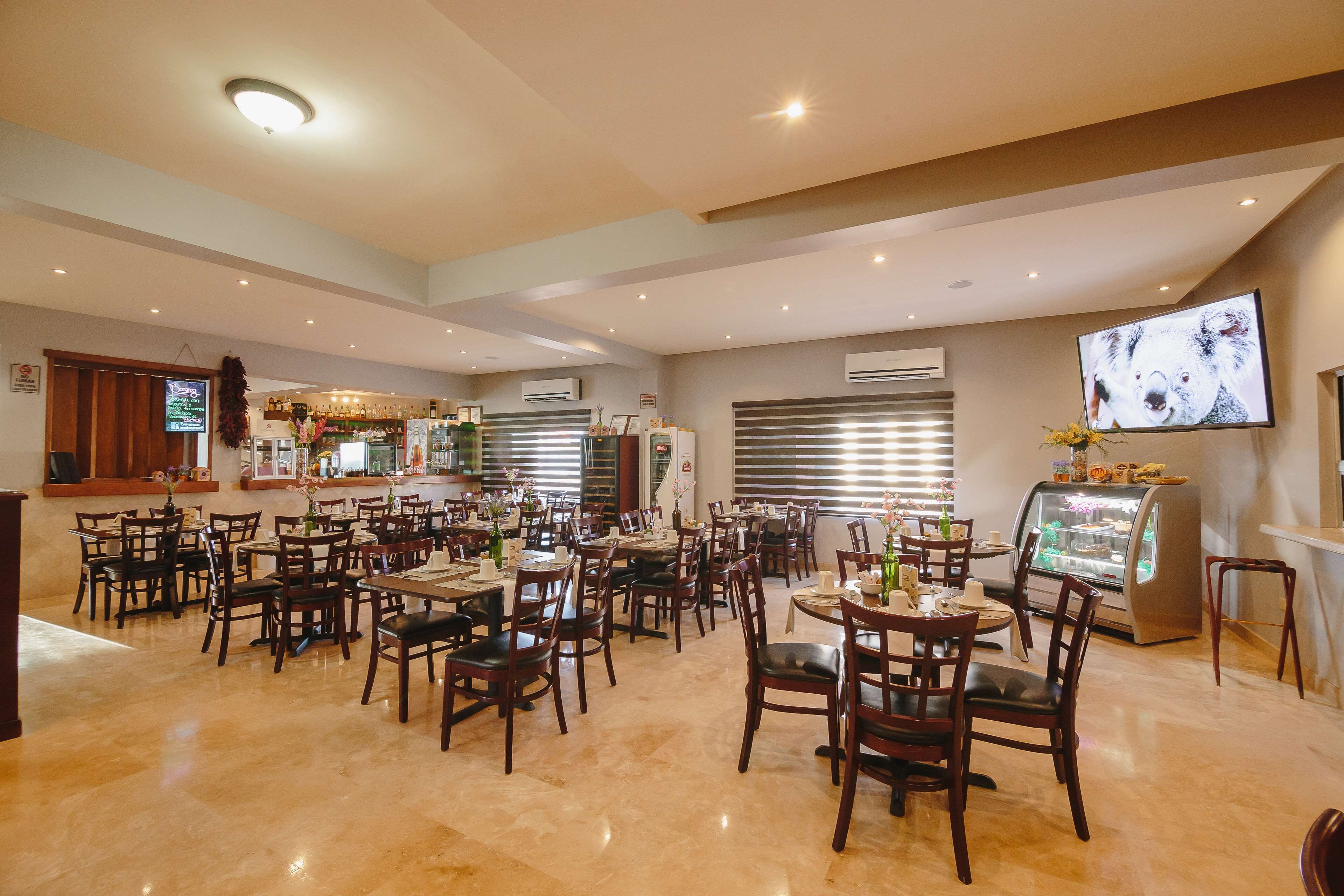 Un restaurante amplio con varias mesas y sillas, una zona de bar y una pantalla de televisión en la pared.