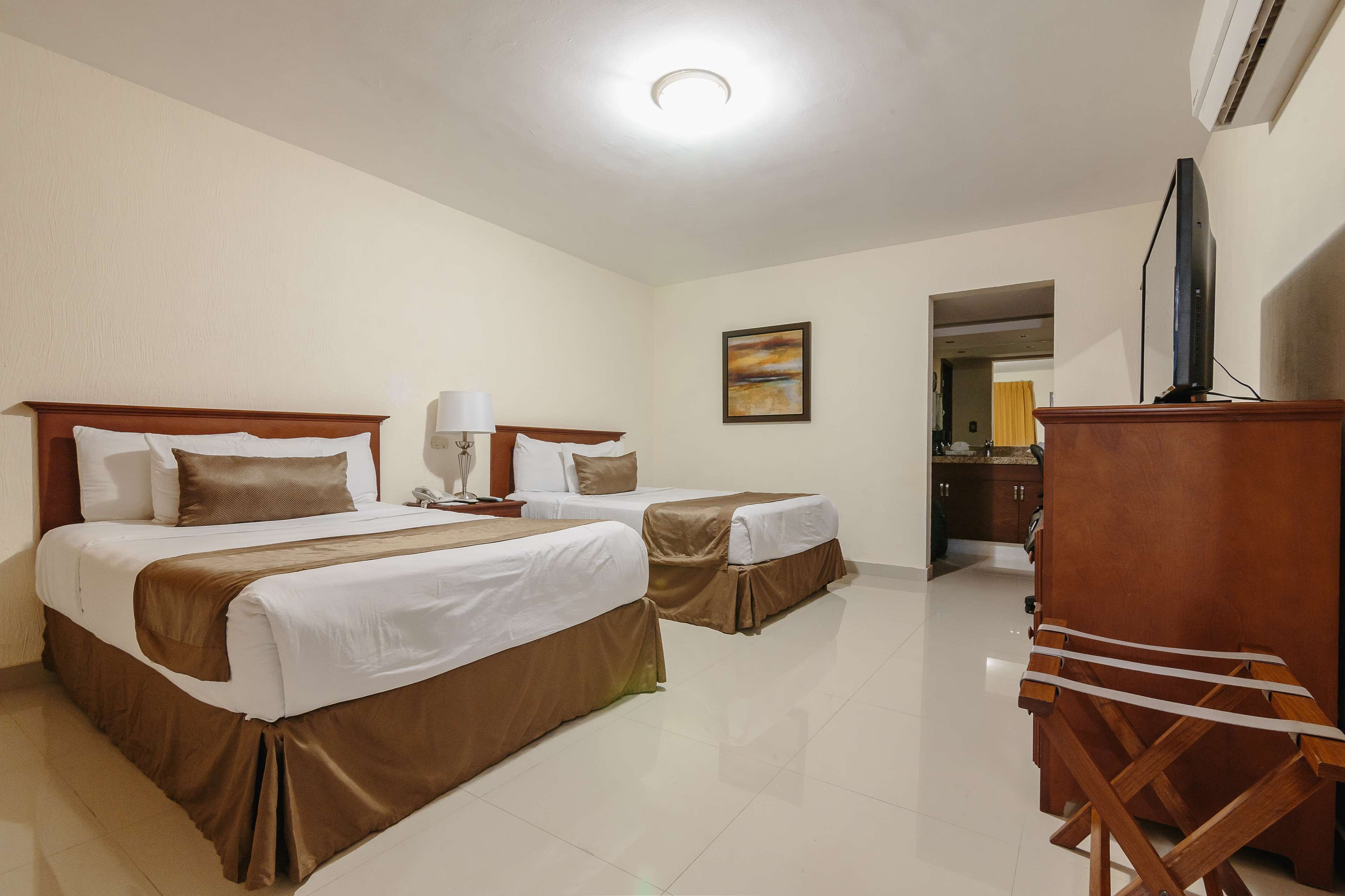 A hotel room with two beds, a TV, a desk, and a mirror.